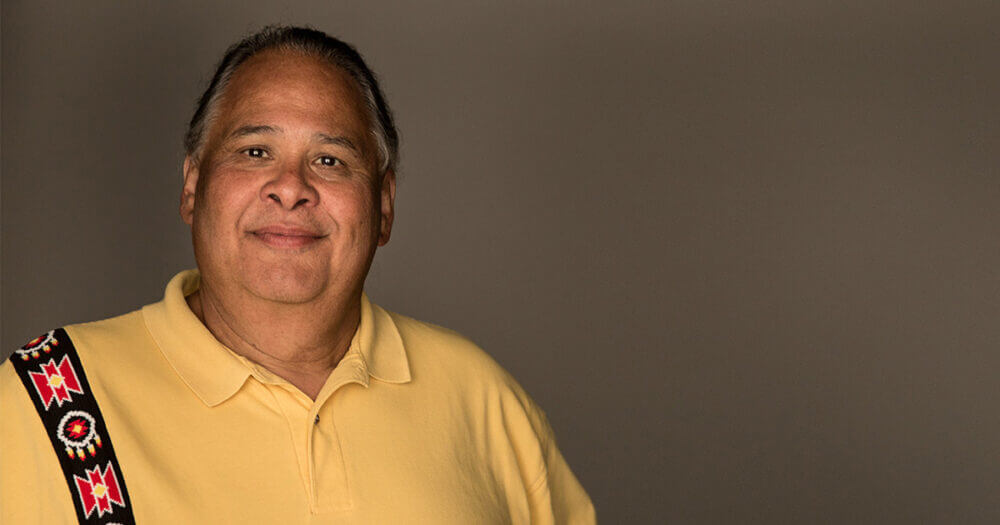 Michael A Goze smiling at camera against a dark gray background